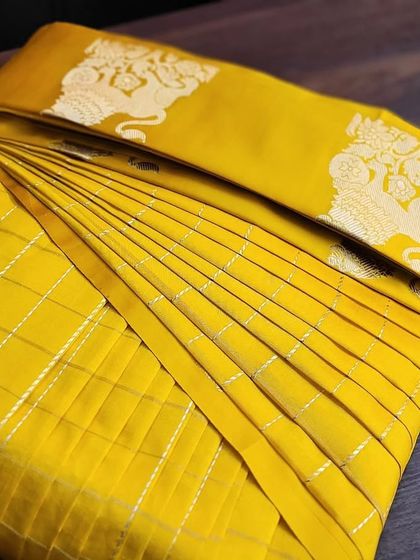 A pre-pleated yellow silk saree, neatly box-folded to protect the fabric and the pleats.