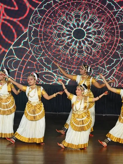 Our Mohiniyattam group performing on a beautifully lit stage with a mandala backdrop. The visual harmony between the dancers and the stage design creates a captivating experience.