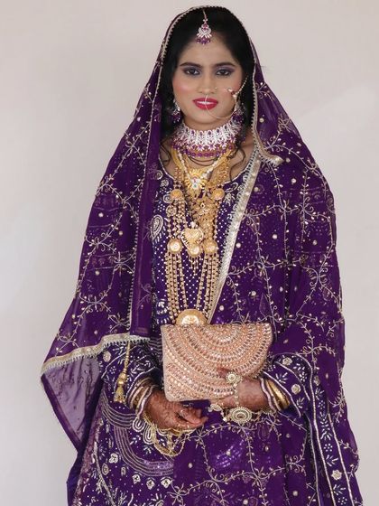 A stunning reception look for a Muslim bride. She is wearing a rich purple outfit with intricate gold embroidery, and her makeup is kept elegant to balance the ornate dress.