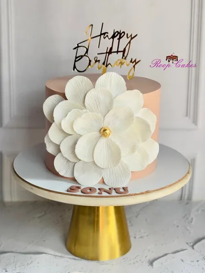 A statement of simple elegance. This cake features a smooth, blush-pink frosting and is adorned with a large, handcrafted white wafer paper flower.