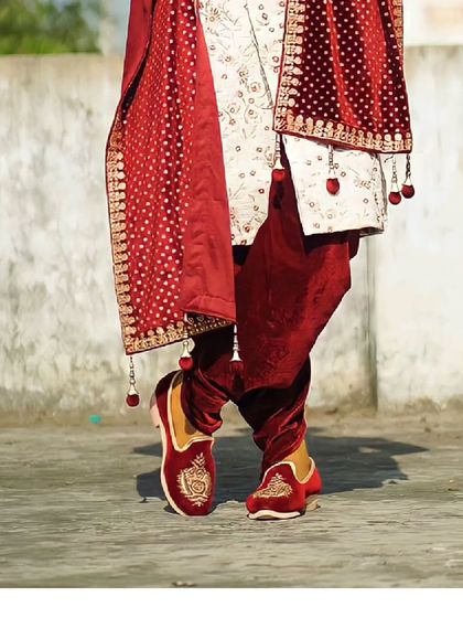 A closer look at the details of a groom's attire. The velvet mojris and the rich red dupatta with tassels add a touch of royalty to the sherwani.