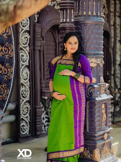 A full-length solo portrait of the mother-to-be in a vibrant green and purple saree, showcasing her beautiful baby bump.