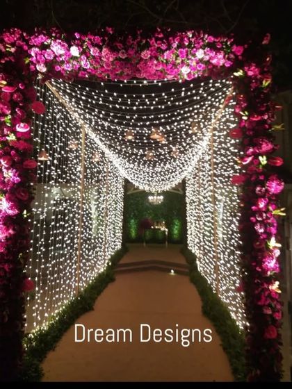 A tunnel of light makes for a truly grand entrance. This walkway is framed by a deep pink floral arch and walls of cascading fairy lights, leading guests into the reception in style.