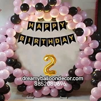 A cute pink and black themed decoration for a second birthday. The balloon arch is accented with a 'Happy Birthday' banner and a golden number '2' foil balloon.