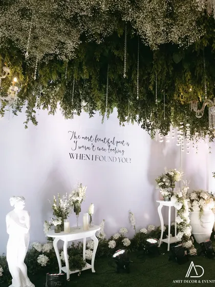 A quiet corner within the grand entrance, featuring a romantic quote, elegant white furniture, and classical statuary, all under a canopy of hanging foliage and crystals.