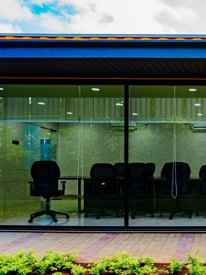 A view into the glass-walled conference room at the Prestige container office. The design emphasizes transparency and openness, connecting the indoor workspace with the surrounding landscaped environment.