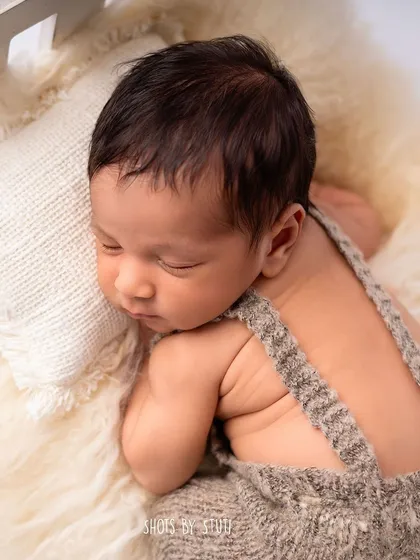 Another angle of this handsome baby boy, showing the texture of the knit outfit and the soft fur he's lying on.