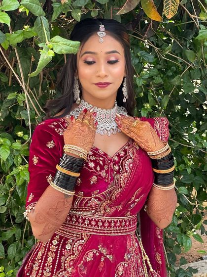 A beautiful outdoor portrait of Pallavi on her reception day. Her red velvet lehenga is paired with a classic glam makeup look, including a defined eye and a deep red lip.