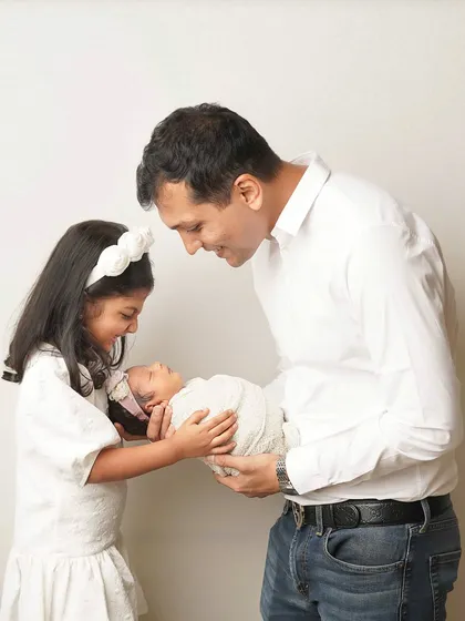 A father and his older daughter share a look as they hold the new baby together. It's a beautiful story of a family growing.