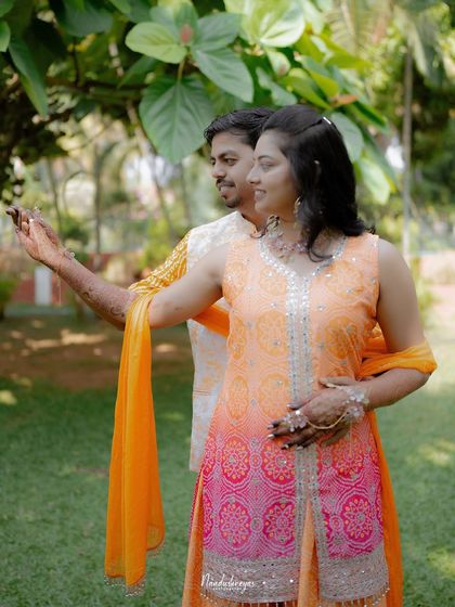 A playful, candid shot of the couple enjoying their outdoor Haldi ceremony. Their natural interaction is the focus, framed by the lush garden setting.