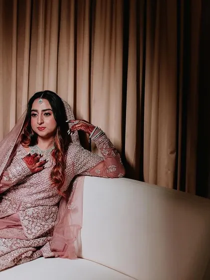 A portrait of a Muslim bride in a stunningly embellished gown, posing elegantly on a white couch.
