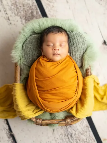 An overhead view of the baby in the basket, showing the full setup with the textured wooden floor and soft green bedding.