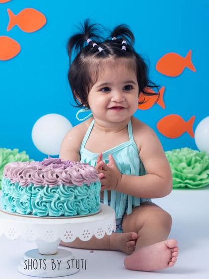 A little mermaid enjoying her first birthday cake. The vibrant blue background and underwater theme details create a magical setting for her celebration.