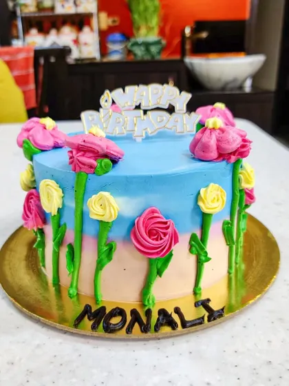 A garden of buttercream flowers. This cake features a pastel sunset-colored base with hand-piped flowers growing up the sides, creating a cheerful and artistic floral design.