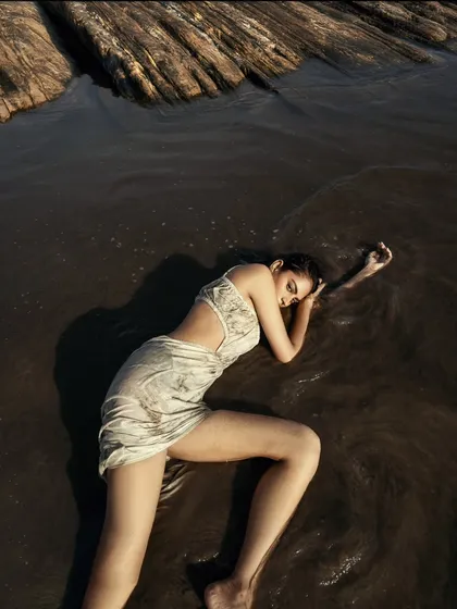 An intimate, poignant pose in the shallow water. This shot focuses on the connection between the model and the natural elements of water and sand.