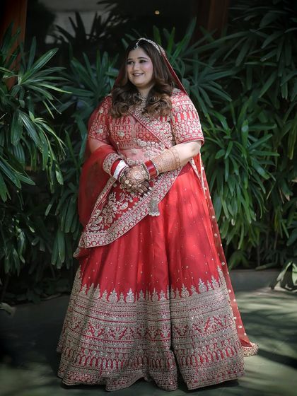 A portrait against a green backdrop, making her red lehenga pop. The makeup is balanced to look great in outdoor, natural lighting.