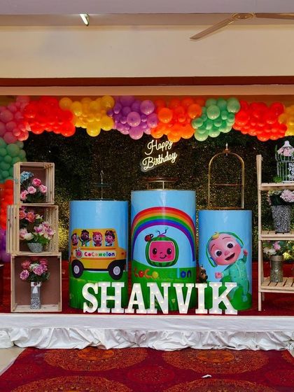 We created this bright and cheerful Cocomelon theme for Shanvik's first birthday. The stage includes character cutouts of JJ and his family, themed pedestals, and a rainbow balloon garland over a green hedge backdrop.