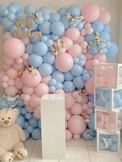 A stunning balloon wall for a gender reveal or baby shower. The wall is packed with pink and blue balloons, with a large teddy bear and 'BABY' blocks adding to the charm.