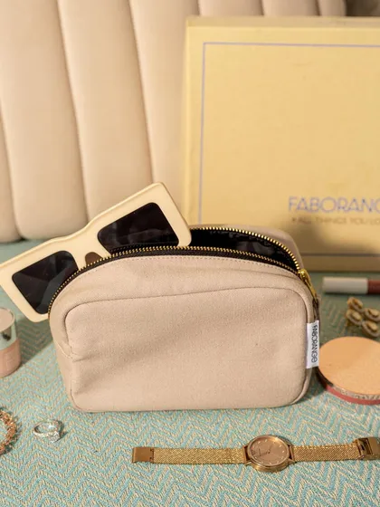A lifestyle flat lay of a Faborange pouch with everyday essentials like sunglasses, a watch, and makeup spilling out. This shot makes the product feel relatable and functional for daily use.