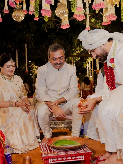 The parents of the groom during the wedding ceremony. The mother wears a stunning ivory and gold saree, complemented by the father's classic bandhgala, creating a look of timeless grace.