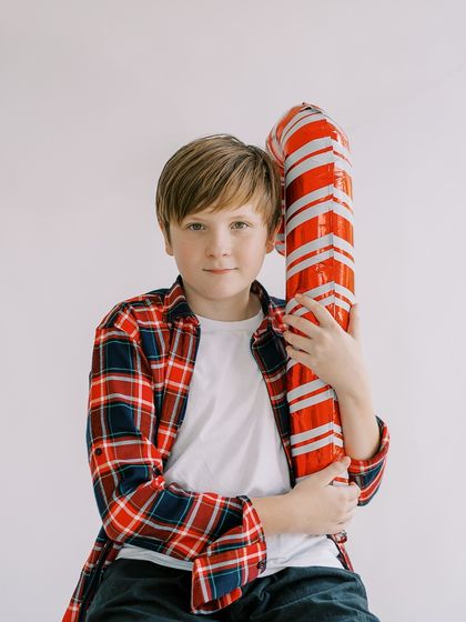 A boy in a plaid shirt holding a giant candy cane. A fun and classic Christmas portrait.