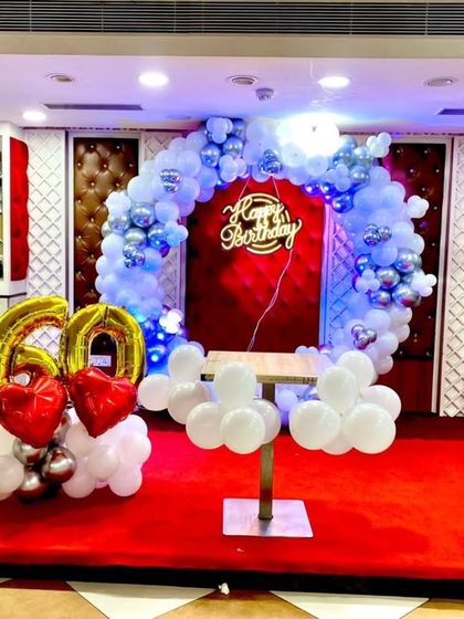 Another view of the 60th birthday setup, showing the stage with the balloon arch, neon sign, and a table for the cake.