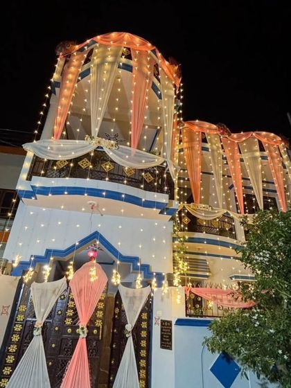 A night view of a home decorated with peach and white drapes and fairy lights. The lighting highlights the beautiful draping and makes the house stand out.