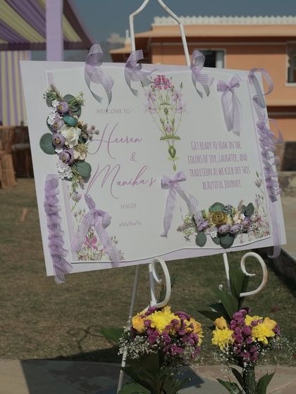 A close-up of the beautifully designed welcome easel, adorned with lavender ribbons and delicate floral illustrations.