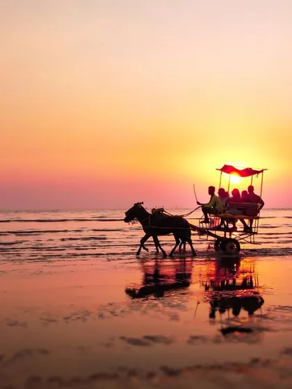 A horse-drawn carriage is silhouetted against a magnificent orange and pink sunset on a Mumbai beach, its reflection visible on the wet sand.