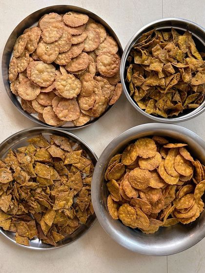 An assortment of my homemade savory snacks in steel bowls, showing the authentic, home-style preparation. Includes different types of mathri and fried crisps.