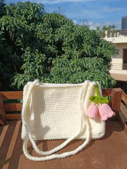 A simple and elegant shoulder bag in off-white, accented with a delicate pink tulip charm. A perfect example of minimalist custom design.