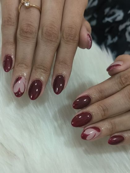 A full view of the maroon heart-themed nails. The combination of the rich, solid color and the creative accent nail makes for a unique and stylish manicure.