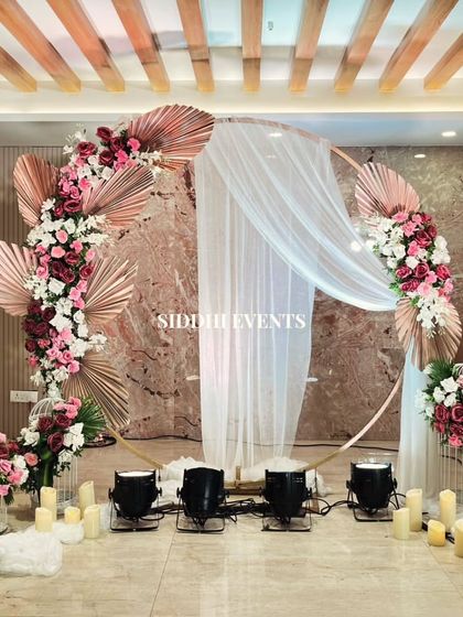 A stunning circular arch adorned with red, white, and pink flowers, with sheer white drapery and candles creating a dreamy and romantic atmosphere for a reception.