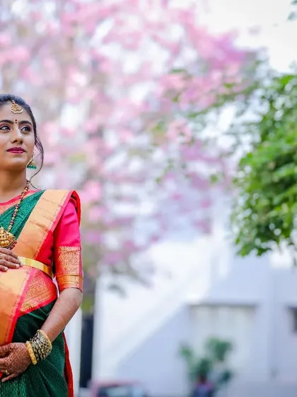A classic solo maternity portrait of a woman in a traditional silk saree, set against a backdrop of pink blossoms. This style is perfect for a Sreemantham or baby shower shoot.