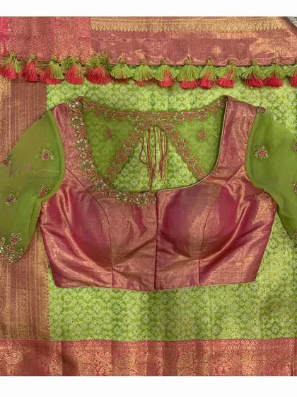 A flat lay of the green and pink saree and blouse, highlighting the double-tassel beaded border and the intricate embroidery.