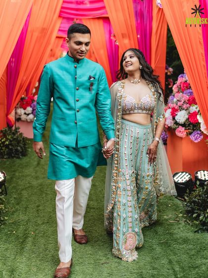 The couple makes their entrance, walking hand-in-hand through a colorful drape-covered walkway, smiling and ready for their Mehendi party.