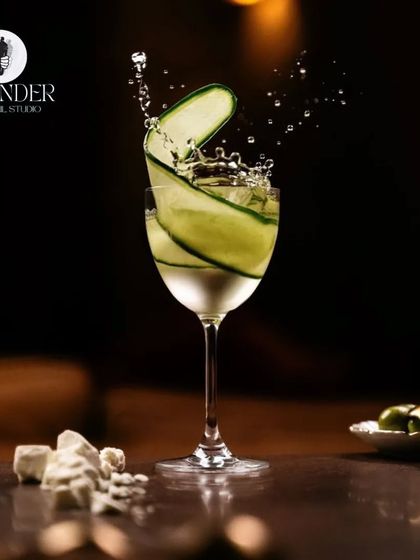 A refreshing gin cocktail with a cucumber ribbon garnish captured in a dynamic splash shot. We create drinks that are both delicious and photogenic.