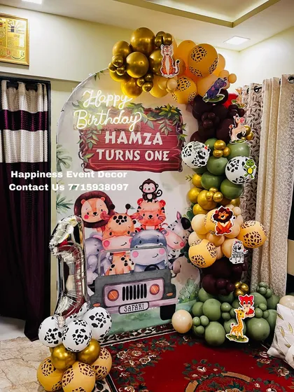 A fun and adventurous jungle safari theme for a first birthday party. This home setup includes a custom backdrop with cute safari animals, a balloon garland in jungle colors, and animal print balloon details.