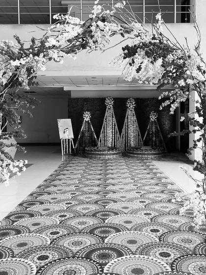 An artistic black and white shot of a wedding reception entrance arch, highlighting the structure and texture of the floral and branch decor.
