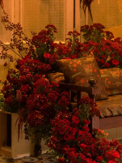 A seating nook overflowing with red blooms. We used custom printed cushions on a traditional wooden bench, surrounded by flowers, to create a beautiful and comfortable spot for guests to relax.