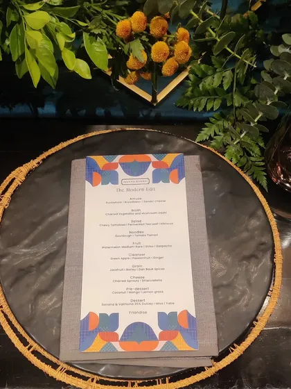 The place setting for the Burma Burma event. A custom-designed menu with vibrant, modern graphics sits atop a woven placemat, perfectly capturing the brand's unique and artistic vibe.