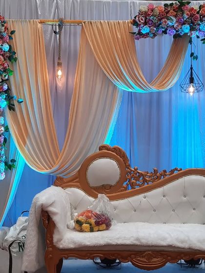 A closer look at the details of a modern engagement stage, focusing on the interplay of the draped fabric, hanging lights, and the elegant white sofa.