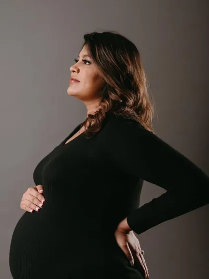 A side profile showcasing her beautiful baby bump. The makeup is elegant and understated, creating a look of pure grace.