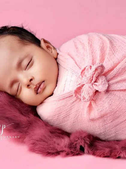 A close-up shot of a sleeping baby, showing the soft texture of the pink wrap and the plush rug.