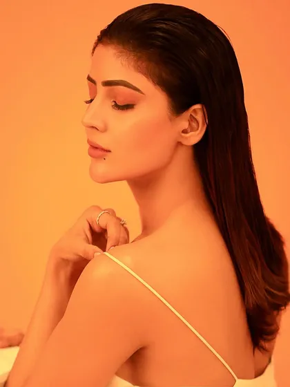 A serene profile shot against a warm, solid-color background. This minimalist approach focuses on the clean lines of the profile, the wet-hair styling, and the soft makeup.