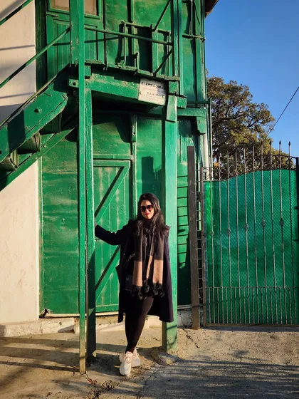 An all-black winter outfit against a vibrant green building in Mussoorie creates a striking visual contrast.