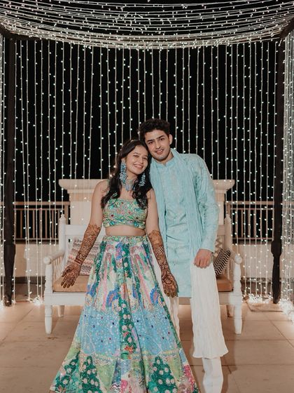 A beautiful portrait of the couple at their Mehendi, posing in front of a stunning wall of fairy lights.