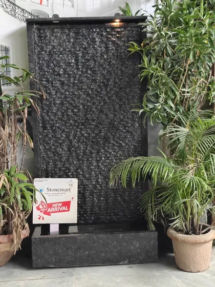 A full view of the 5-foot granite waterfall, surrounded by plants. Its slim profile makes it ideal for patios, balconies, or against a feature wall.