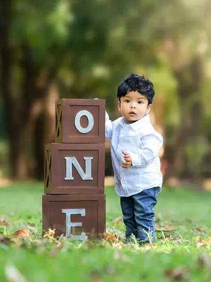 A toddler stands proudly next to "ONE" blocks during an outdoor first birthday photoshoot. Outdoor sessions offer beautiful natural light and a different environment for capturing milestones.