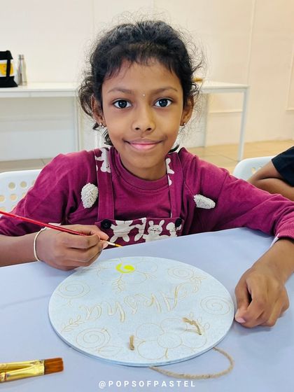 A young artist carefully paints her nameplate at a kitty party, a fun activity that also serves as a personalized party favor.